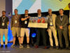 Spaceflower zahlt Games-Förderung für ‚Let Them Trade‘ zurück Scheck is back: Digitalminister Fabian Mehring mit dem Spaceflower-Team und Vertretern des FFF Bayern beim Bayerischen Digitalgipfel 2026 am 25. Juni in Nürnberg.